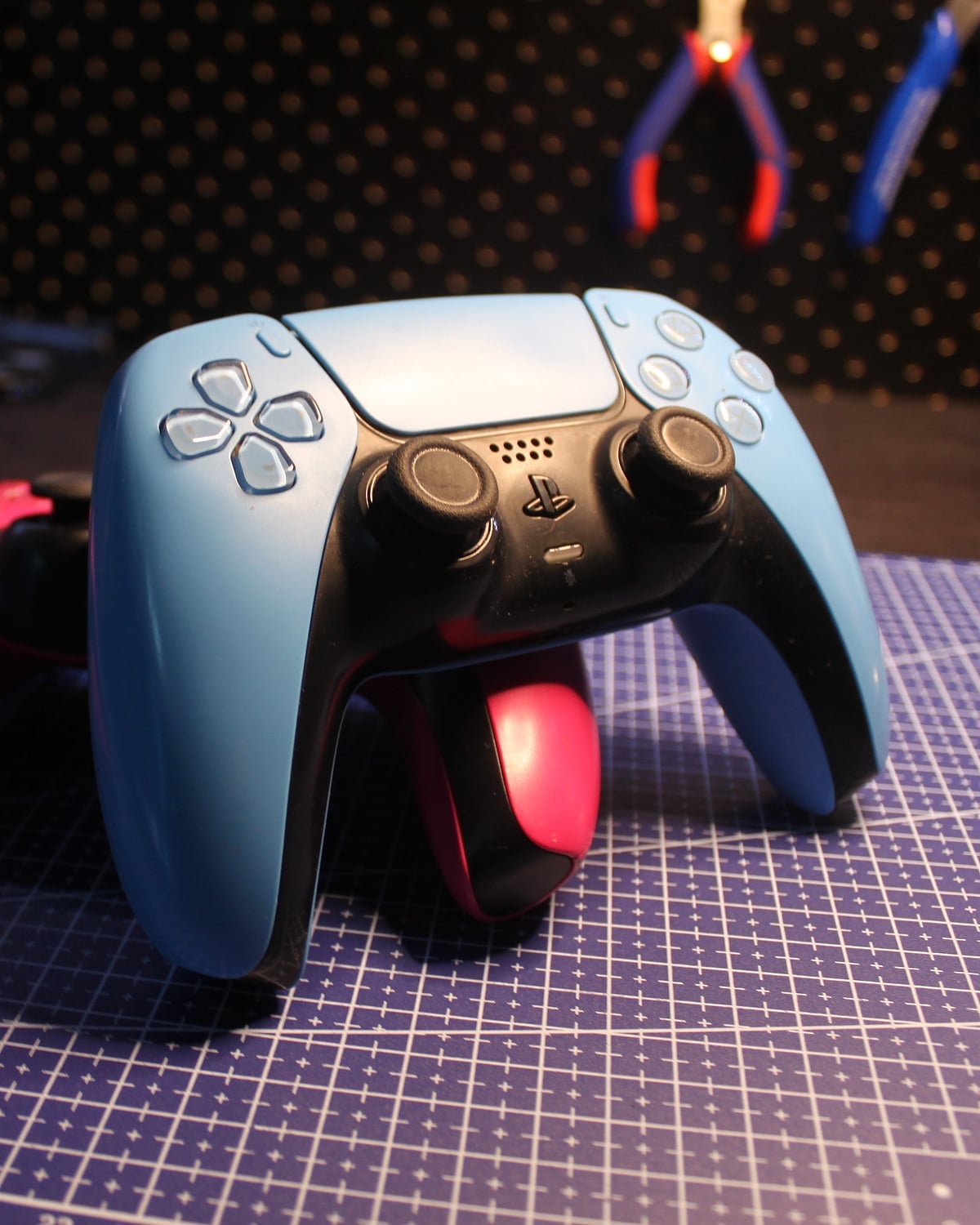 A blue DualSense controller in front of two pink ones on the workbench